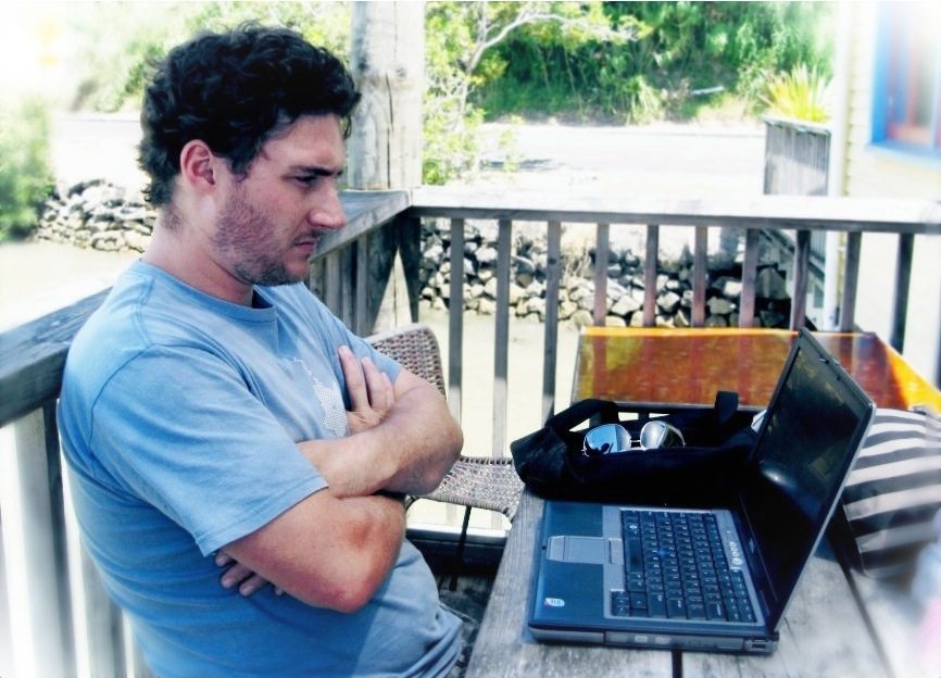 A man waits on a rural porch for a website to load on his Dell laptop.